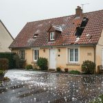 Maison individuelle française après un violent orage de grêle, avec des tuiles endommagées et des grêlons visibles au sol.