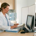 Médecin dans un cabinet moderne, organisant des dossiers près d’un ordinateur sécurisé, dans une ambiance professionnelle et rassurante.
